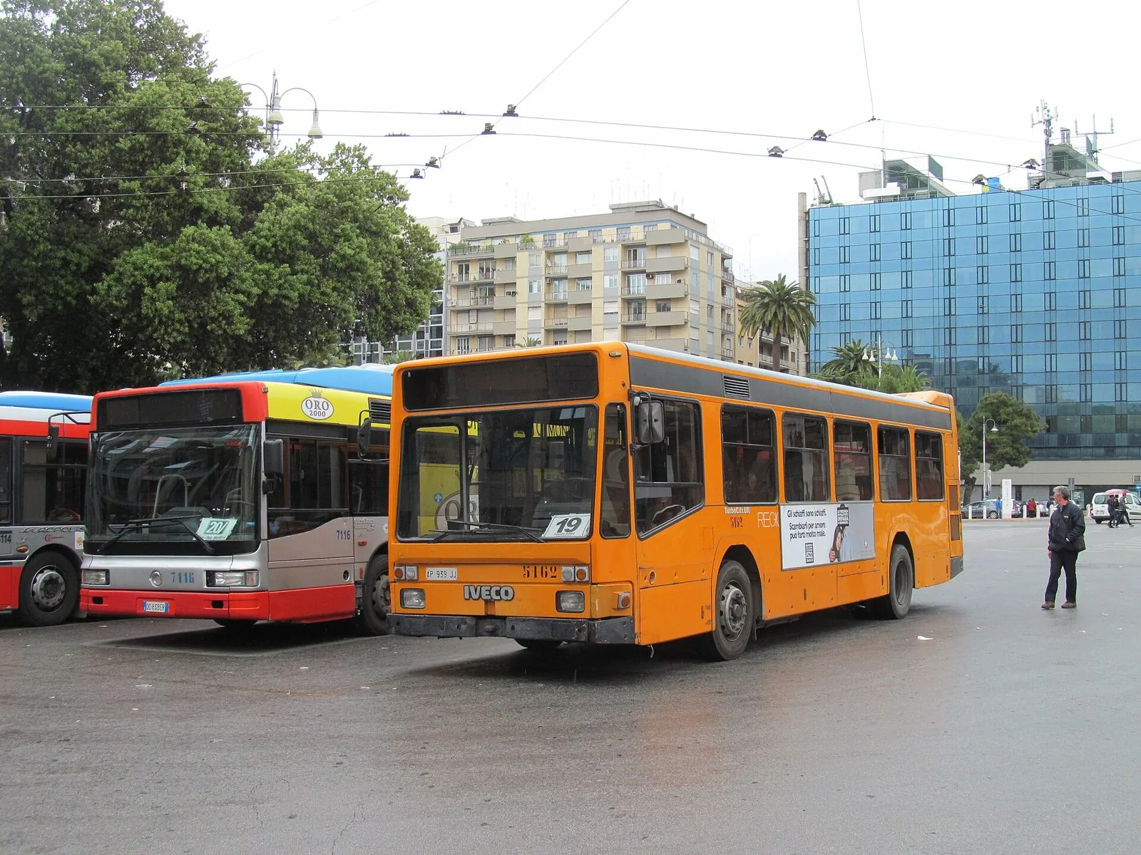 Autobus urbani in sosta in piazza Aldo Moro a Bari, davanti alla stazione centrale, con un bus arancione della linea 19 in primo piano