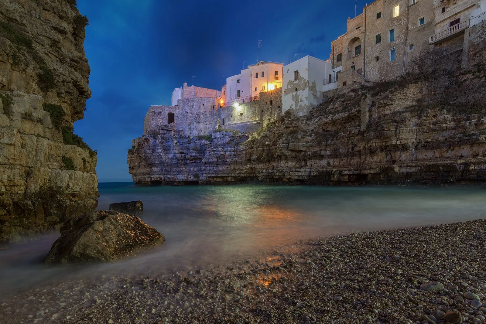 La cala di Lama Monachile a Polignano a Mare all'imbrunire, con la spiaggia di ciottoli e le case del centro storico sulla scogliera illuminate